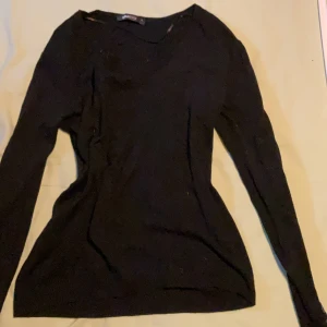 Svart tröja med knappar från Gina Tricot - Svart tröja från Gina Tricot i storlek S. Tröjan har långa ärmar, v-ringning och små knappar på ärmarna. Enkel och stilren modell som är lätt att matcha. Perfekt för lager-på-lager och funkar året runt.