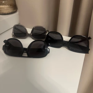Tre par stora solglasögon - Säljer tre par trendiga solglasögon med stora bågar. Två par är svarta med fyrkantig form och ett par är transparent grå. Alla har mörka glas och plastbågar, perfekta för att lyfta din look i sommar.