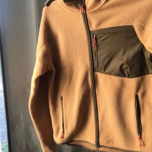 Svart och grå fleeceväst Peak Performance - Säljer en riktigt snygg fleeceväst från Peak Performance med svart och grått mönster. Västen har en stor bröstficka med dragkedja och Peak Performance-logga, samt hel dragkedja framtill. Perfekt lager-på-lager-plagg för kyliga dagar. Har fått dom i födelsedagspresent men har tagit beslutet på att jag inte vill ha dom. Priset går att diskutera. Dom är helt nya och oanvända. Kvitto finns!