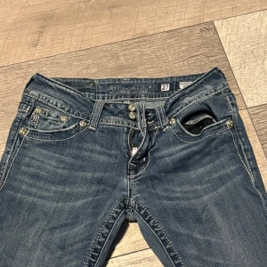 Miss Me jeans med strassdetaljer - Om ni bor i Stockholm kan vi mötas istället och få billigare Snygga blå Miss Me jeans med låg midja och raka ben. Jeansen har coola strassdetaljer på bakfickorna, dubbla knappar och snörning fram. Klassisk denim med kontrastsömmar och metallknappar för en extra edgy look.