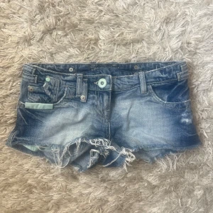 Blå slitna jeansshorts med fransar - Snygga blå jeansshorts med slitna detaljer och fransig kant. Klassisk femficksmodell med ljus tvätt och coola slitningar framtill och baktill. Perfekta för sommaren och ger en avslappnad vibe.