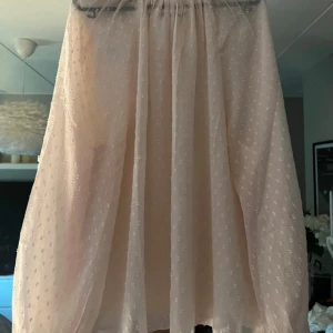 Ljusrosa långkjol i tunn bomull - Superfin ljusrosa långkjol i tunn, transparent bomull med diskret prickigt mönster. Kjolen har ett flowy fall och resår i midjan för en bekväm passform. Perfekt för varma dagar när du vill ha en luftig och söt look.