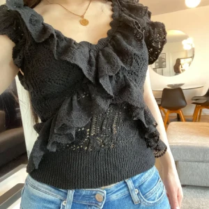 Svart blus med volanger  - Supersnygg svart blus från Zara med v-ringning, volanger och spetsdetaljer. Toppen är ärmlös och har en croppad passform med ribbad midja. köpt för längesedan men endast testad, storlek M men passar mig med S/XS också.