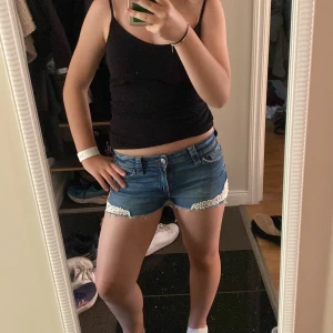 Jeansshorts med spets från H&M - Snygga blå jeansshorts från H&M med vit spetsdetalj nertill. Klassisk femficksmodell med låg midja och dragkedja. Perfekta för sommaren och ger en chill vibe till din outfit. Har använt 1 gång