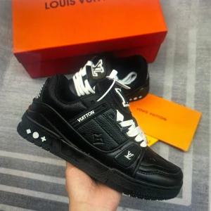 Svarta Louis Vuitton sneakers - Snygga svarta sneakers från Louis Vuitton med vita snören och ikoniska LV-detaljer. Skorna har en chunky sula, präglad logga på sidan och är tillverkade i skinn med stilrena kontraster. Perfekta för dig som vill sticka ut med lyxig streetstyle.