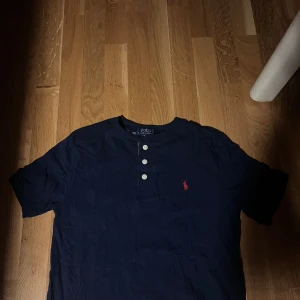 Mörkblå t-shirt från Polo Ralph Lauren - Säljer denna tröja då den är för liten och helt enkelt inte är i min stil. Den är mörk blå med en röd Ralph Lauren logga.   Storlek L i barn storlek men passar även som storlek S i vanlig storlek.   Kontakta vid frågor eller pris