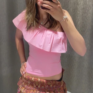 Rosa offshoulder topp med volang - Jättefin one shoulder topp från Kappahl! Den är i nyskick och har fortfarande taggen på! Vid frågor eller funderingar så är det bara att höra av sig! Den sitter som en storlek Xs i dam men är originellt 134-142 i barnstorlek. Ni kan se hur den sitter på, på bilden! 💕
