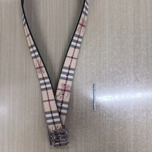 Burberry rutigt skärp med silverdetalj - Snyggt Burberry-bälte i klassiskt beige och vinrött rutigt mönster med silverfärgat spänne. Ena sidan har den ikoniska rutan, andra sidan är svart. Tillverkad i skinn och levereras med originalpåse och box. Perfekt accessoar för att lyfta din outfit.
