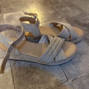 Beige sandaler med platåsula - Snygga beige sandaler med korsade remmar i mocka och justerbart spänne vid ankeln. Skorna har en plattformsula med flätad detalj som ger en chill sommarkänsla. Perfekta för varma dagar och lätta att matcha med allt.
