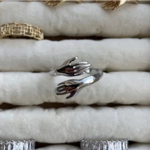 Silvrig ring med handmotiv - Unik silvrig ring med två händer som möts framtill. Ringen har en cool och modern design som sticker ut och passar perfekt för dig som gillar statement-smycken. Justerbar storlek och blank finish.