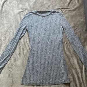 Grå ribbad långärmad tröja från SHEIN - Slimmad grå långärmad tröja med ribbat mönster och rund hals. Mjuk och stretchig, perfekt att styla med jeans eller kjol. Materialet känns lätt och följsamt, och den har en enkel men snygg look som funkar året runt.