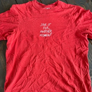Röd t-shirt Pull&Bear med tryck - Röd t-shirt från Pull&Bear i bomull med vit text på bröstet: 'Save it for another moment'. Klassisk rund hals och korta ärmar. Perfekt för dig som gillar enkel men snygg stil. Köpt i Bali