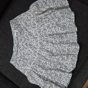 Grå/grön blommig volangkjol - Supersöt grå/grön kortkjol med vita blommor och volangkant. Kjolen har en avslappnad passform och är perfekt för varma dagar. Väldigt stretchigt material.