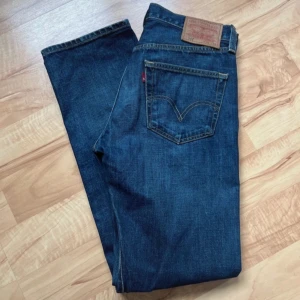 Blå jeans Levi's 501 - Säljer ett par klassiska blå jeans från Levi's med fem fickor och en rak passform. De har en traditionell design med en läderpatch baktill och den ikoniska röda etiketten på bakfickan. Perfekta för en avslappnad stil.