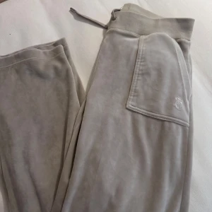 Beige mjukisbyxor från Juicy Couture - Säljer ett par bekväma beige mjukisbyxor från Juicy Couture. Byxorna har en elastisk midja med snörning och en praktisk bakficka med knappar. Perfekta för en avslappnad stil.
