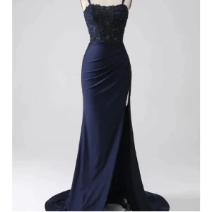 Mörkblå balklänning med spetsdetaljer - Elegant mörkblå långklänning/balklänning med spetsdetaljer och smala axelband. Klänningen har en vacker slits och snörning i ryggen för en perfekt passform. Perfekt för speciella tillfällen eller till din bal. Helt oanvänd, lappen är kvar.