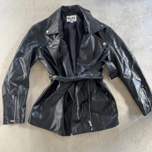 Svart skinnjacka från NA-KD - Svart skinnjacka från NAKD med bälte i midjan, stl 34