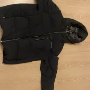 Svart dunjacka från Parajumpers - Säljer en svart dunjacka från Parajumpers med en cool patch på ärmen. Jackan har en dragkedja framtill och en huva för extra skydd. Perfekt för kyliga dagar.har lite tyg lossnat på fram sidan går att sy. Bra 