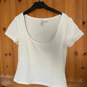 Vit kortärmad topp från H&M - Säljer en enkel och stilren vit kortärmad topp från H&M. Perfekt basplagg med rund halsringning, tillverkad i mjukt material för en bekväm passform. Passar till många olika outfits!