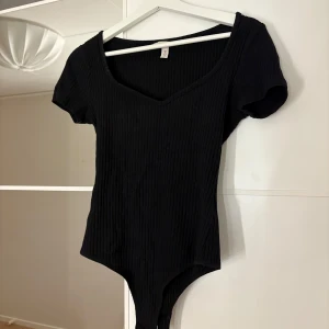 Svart ribbad bodysuit - Snygg svart ribbad bodysuit från H&M med korta ärmar och v-ringning. Hör av er vid funderingar eller om ni vill ha bilder med hur plagget sitter på mig. Titta gärna in mina andra plagg!