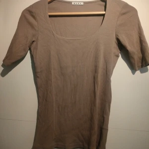 Beige ribbad topp från Wera - Säljer en stilren beige/brun ribbad topp från Wera. Toppen har en fyrkantig halsringning och korta ärmar, perfekt för en avslappnad look. Passar bra till både jeans och kjol.