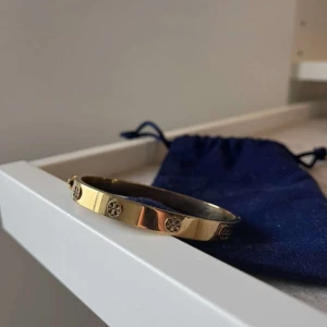 Tory brunch guldarmband  - Elegant guldarmband med dekorativa runda detaljer. Armbandet har en stilren design och kommer med en mörkblå förvaringspåse. Perfekt för att ge en touch av lyx till din stil.