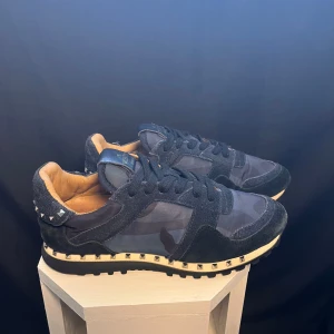 Valentino Garavani sneakers i blått - Snygga Valentino Garavani sneakers i blått med camouflagemönster och nitar på hälen. Skorna har en klassisk snörning och en bekväm innersula. Perfekta för en stilren look.