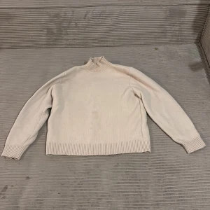 Vit stickad polotröja - Säljer en stilren vit stickad polotröja med ribbade detaljer vid krage, ärmslut och nederkant. Perfekt för kyligare dagar och ger en klassisk look. Passar bra till både jeans och kjol.