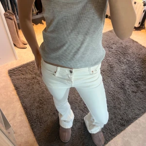 Vita jeans låga bootcut  - Snygga vita jeansbyxor med låg midja och bootcut-stil. Perfekta för en stilren look. De har klassiska fem fickor och knappar i midjan.