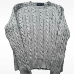 Grå stickad tröja från Ralph Lauren - Säljer en stilren grå stickad tröja från Ralph Lauren med klassiskt flätmönster. Tröjan har en broderad logotyp på bröstet och ribbstickade muddar vid ärmslut och nederkant. Perfekt för kyliga dagar!