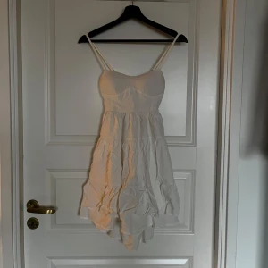 Vit klänning från Dennis Maglic - Söt vit klänning från Dennis Maglic med smala axelband och en luftig kjol. Klänningen har en öppen ryggdetalj och är perfekt för varma dagar. Den är tillverkad i ett lätt material som ger en skön känsla.