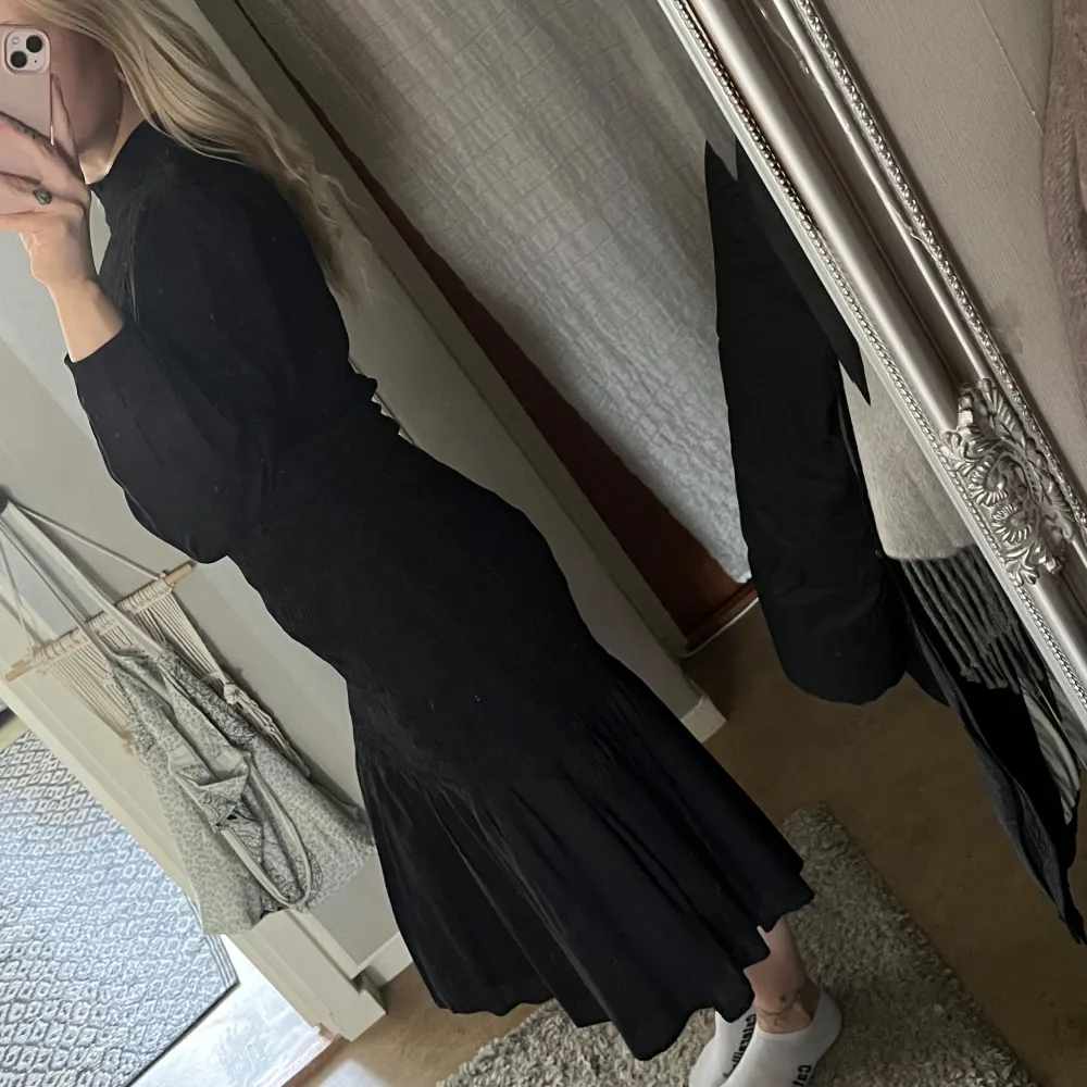 Elegant svart stretchig långklänning med smockdetaljer upptill och långa ärmar. Perfekt för en stilren look. Klänningen har en rund hals och ett flytande fall som ger en vacker silhuett. 100% eko viskos. Strl S . Mekot.