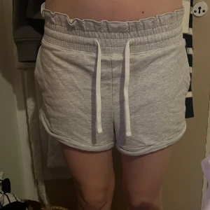 Grå mjukisshorts från Hollister - Säljer ett par grå mjukisshorts från Hollister med elastisk midja och snörning. Shortsen har en bekväm passform och slits på sidorna för extra rörelsefrihet. Perfekta för en avslappnad stil.