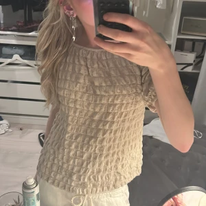 Beige topp från Zara - Säljer en beige topp från Zara med ett unikt texturerat mönster. Toppen har korta ärmar och en lös passform, perfekt för en avslappnad stil. Tillverkad i ett mjukt och bekvämt material.