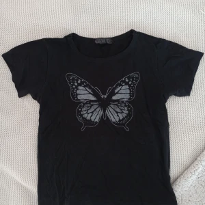 Baby tee med fjäril - Säljer denna svarta babytee med fjärilstryck. Passar XS/XXS och sitter tight💕 Perfekt för dig som tycker om kläder från tidigt 2000-tal! 