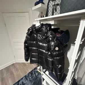 Moncler maya down jacka - Säljer en snygg svart dunjacka från Moncler. Jackan har en glansig finish och är utrustad med dragkedja. Perfekt för kalla dagar med sin varma och stilrena design. Moncler-logga på ärmen ger en exklusiv touch. Det är storlek 1 vilket motsvarar S ungefär 
