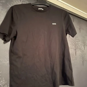 Svart t-shirt från BOSS - Säljer en stilren svart t-shirt från BOSS med liten logga på bröstet. Inga skador eller liknande. Storleken är S. Priset är inte hugget i sten. Hör av er vid minsta fråga!