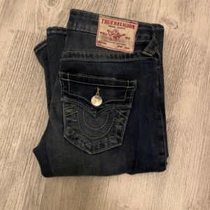 Mörkblå bootcut jeans från True Religion - Snygga mörkblå bootcut jeans från True Religion med ikonisk bakficka och kontrastsömmar. Jeansen har en låg midja och klassisk femficksdesign. Använd 2 gånger och i perfekt skick. Ny pris 1300.