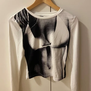 Svartvit långärmad topp med tryck - Snygg svartvit långärmad topp med ett unikt tryck. Perfekt för att ge din outfit en cool och modern touch. Toppen har en tight passform och är tillverkad i ett mjukt material för extra komfort.