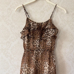 Leopardmönstrad klänning från Bardot Junior (8) - Snygg leopardmönstrad klänning från Bardot Junior med volangdetaljer. Klänningen har smala axelband och en luftig passform, perfekt för en trendig look. Den är tillverkad i ett lätt och bekvämt material.