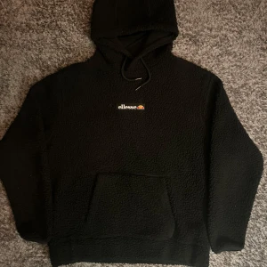Svart fleece hoodie från Ellesse - Mysig svart fleece hoodie från Ellesse med broderad logga på bröstet. Perfekt för kyliga dagar med sin varma och bekväma design. Storlek: men passar även S 