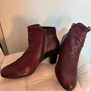 Vinröda stövletter med dragkedja - Snygga vinröda stövletter med dragkedja och klack. Tillverkade i skinn med en elegant spetsig tå. Perfekta för att ge en stilfull touch till din outfit.