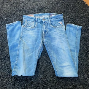 Blå jeans från Replay - Säljer ett par snygga blå jeans från Replay i modellen Anbass. De har en klassisk femficksdesign med dragkedja och knapp. Jeansen har en lätt tvättad look och är perfekta för en avslappnad stil.