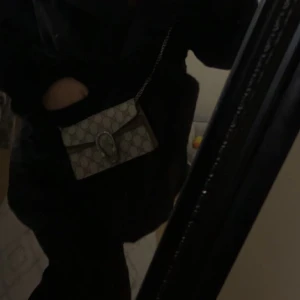 Mönstrad axelväska med kedja - Snygg axelväska med kedja och ett stilrent mönster. Väskan har en unik spänne framtill och är perfekt för att lyfta din outfit. Den är kompakt men rymmer det viktigaste du behöver ha med dig. Serie nummer finns i väskan 