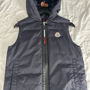 Moncler väst - Säljer nu min riktigt snygga Moncler väst i storlek 14y passar smal i herrstorlek!😃 finns äktehets certifikat från garmsmarket! 9-10 i skick inga fläckar eller defekter! Mitt pris endast 1499✌🏻