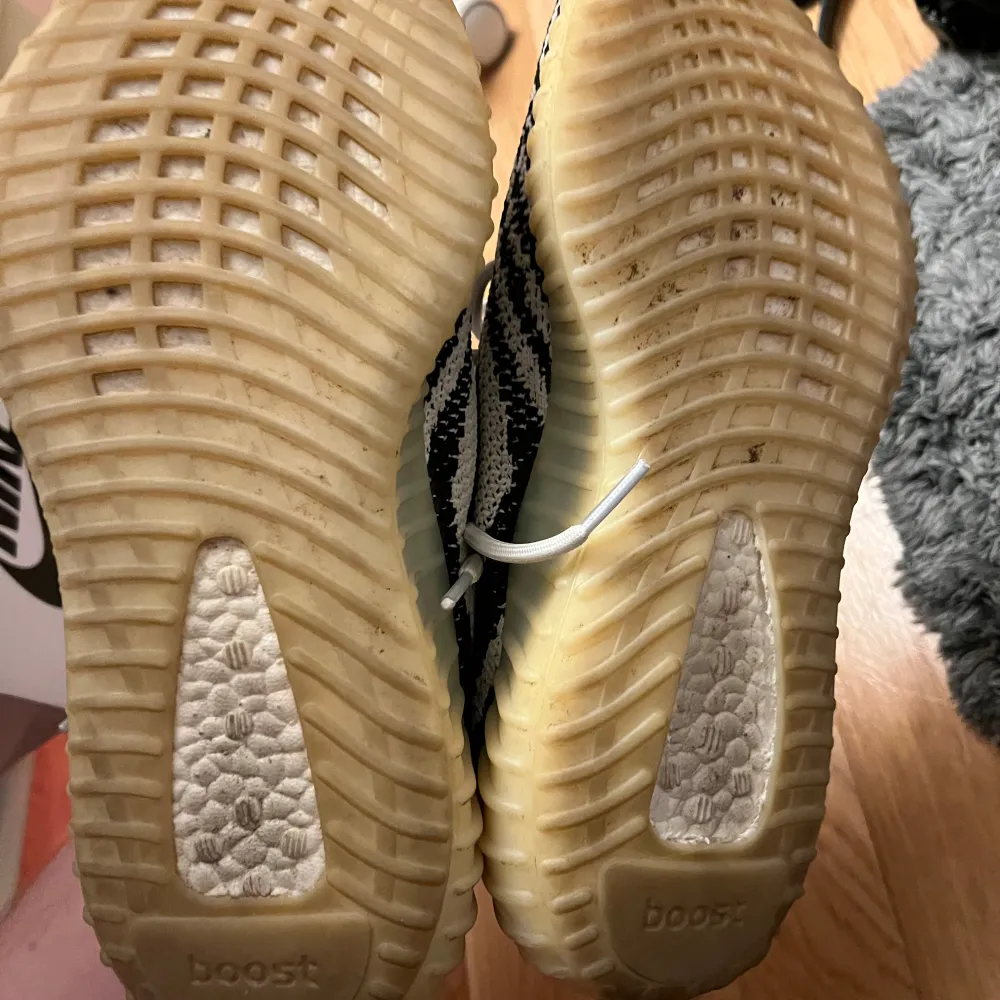 Säljer ett par Adidas Yeezy Boost 350 V2 i den populära 'Zebra' färgkombinationen. Skorna har en vit och svart randig design med röd text på sidan. De har en bekväm och dämpande sula, perfekt för både stil och komfort. Skicket är använt. Kengät.