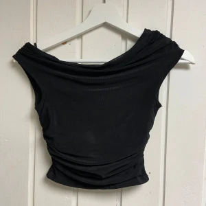 Svart offshoulder topp - Snygg svart offshoulder topp med draperad design. Perfekt för en stilren look. Toppen har en tight passform.