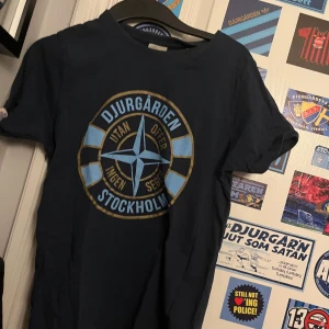 Blå t-shirt med Djurgården-tryck - Snygg blå t-shirt med stort Djurgården-tryck i blått och gult på framsidan. Perfekt för alla Djurgården-fans som vill visa sitt stöd. T-shirten har en klassisk passform och korta ärmar.
