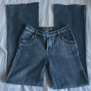 Blå jeans från Bonny Girl - Snygga blå jeans från Bonny Girl med unika detaljer på bakfickorna. De har en klassisk femficksdesign och en knapp med texten 'Sport Casual'. Perfekta för en avslappnad stil.