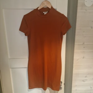 Orange ribbad klänning från Monki - Snygg orange ribbad t-shrit-klänning från Monki i storlek M. Den har en kort och figurnära passform med korta ärmar. 